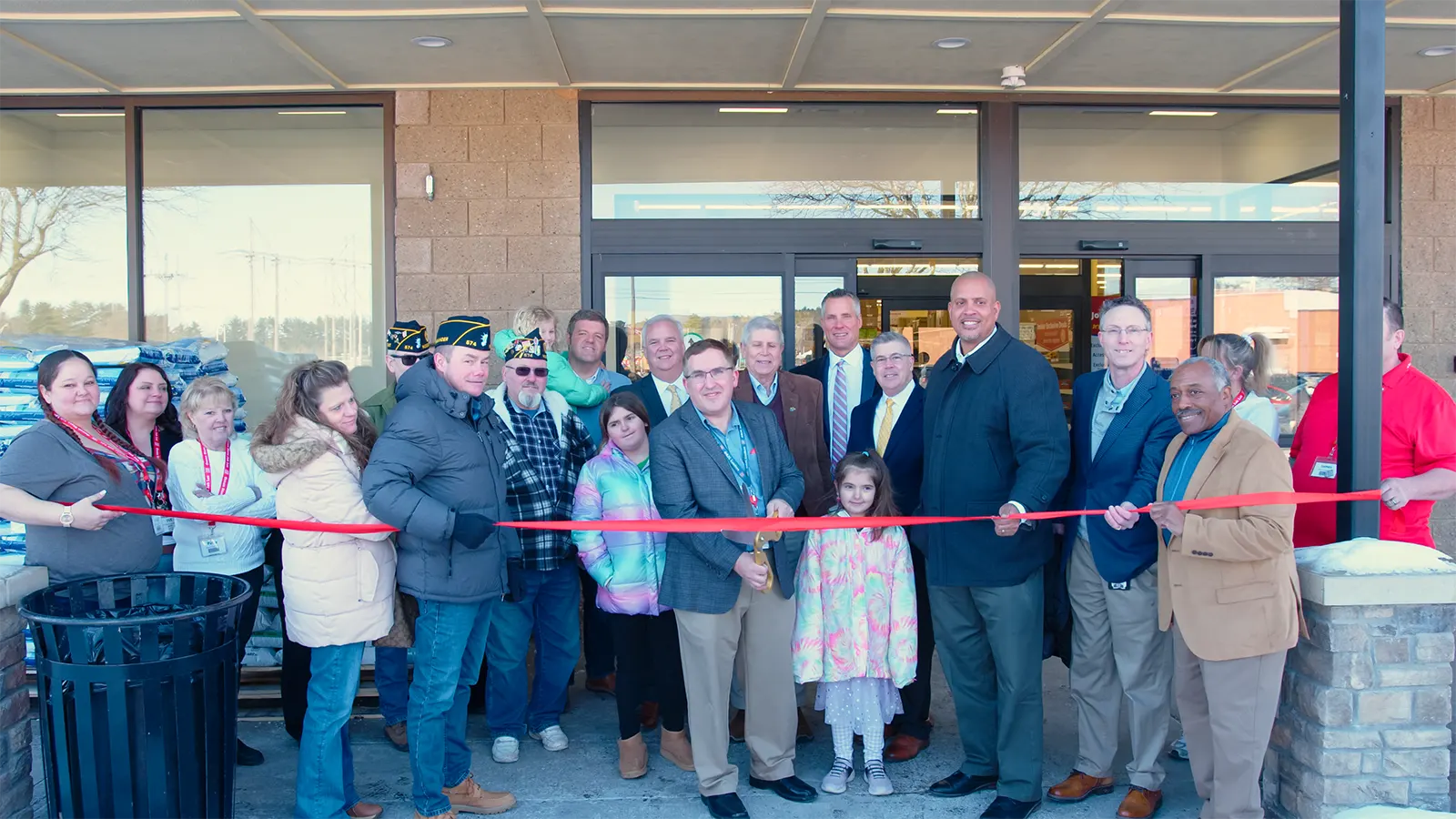 Store Team Leader Bill Mapes cutting the ribbon surrounded by additional OSJL representatives and store associates , local dignitaries, and representatives from the American Legion Hudson Falls Post 574.