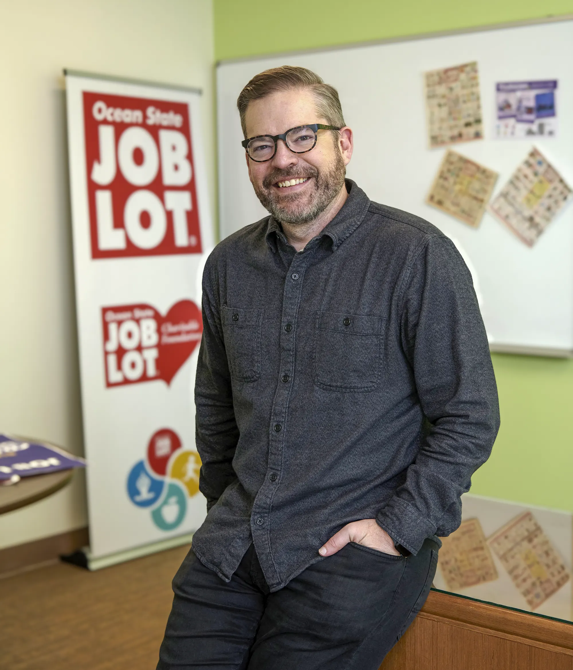Ocean State Job Lot new CMO Luke Estep leaning on his desk in his office.